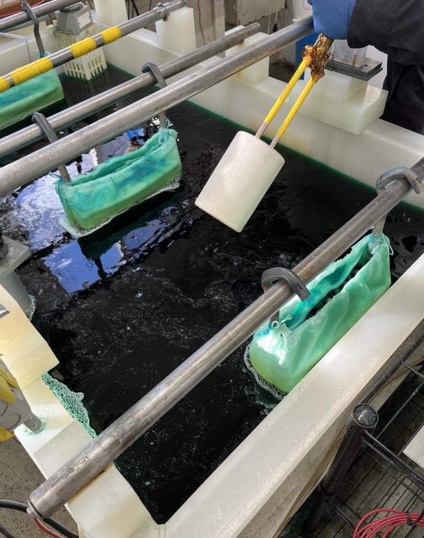 Gloved hand holding a white 3D printed polymer form above an electroforming tank