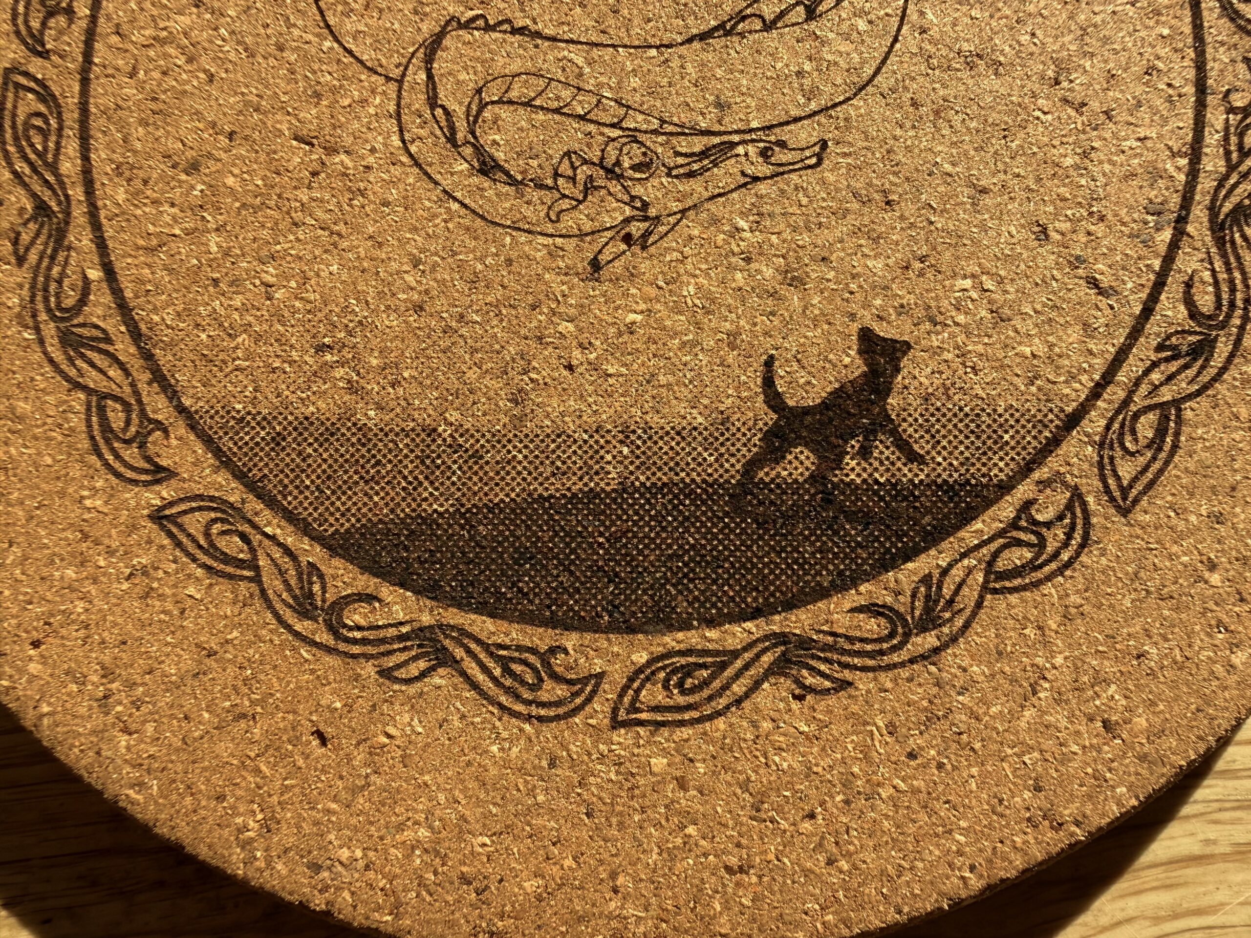 Close-up of the cork coaster showing the dithered ground, the dog silhouette and the border line work