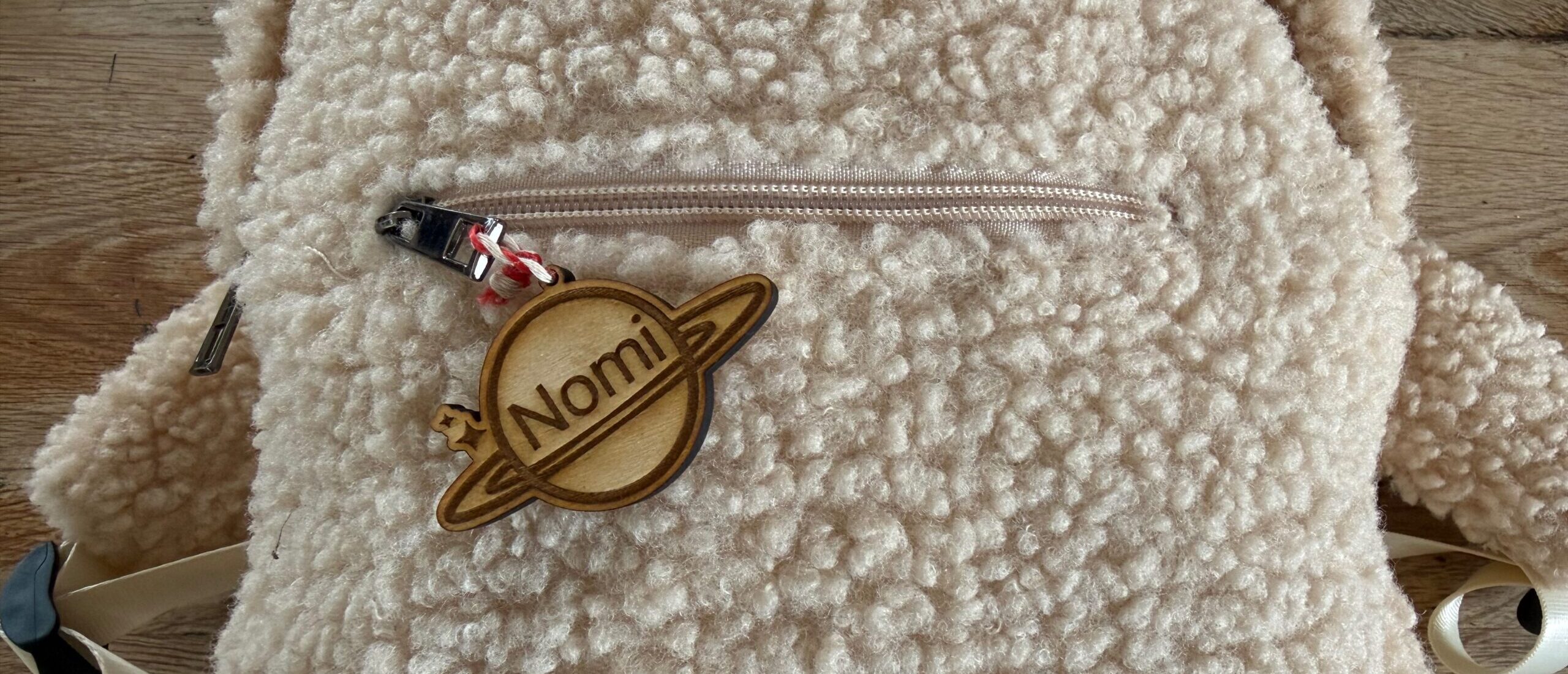 A plywood keychain shaped like a ringed planet, cut on the Creality Falcon A1C, hanging from a child's backpack