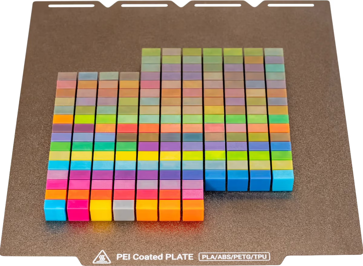 A grid of more than a hundred small color swatch blocks printed on a PEI build plate, blended from the four Full Spectrum filaments with the cyan, magenta, yellow and gray base colors in the front row