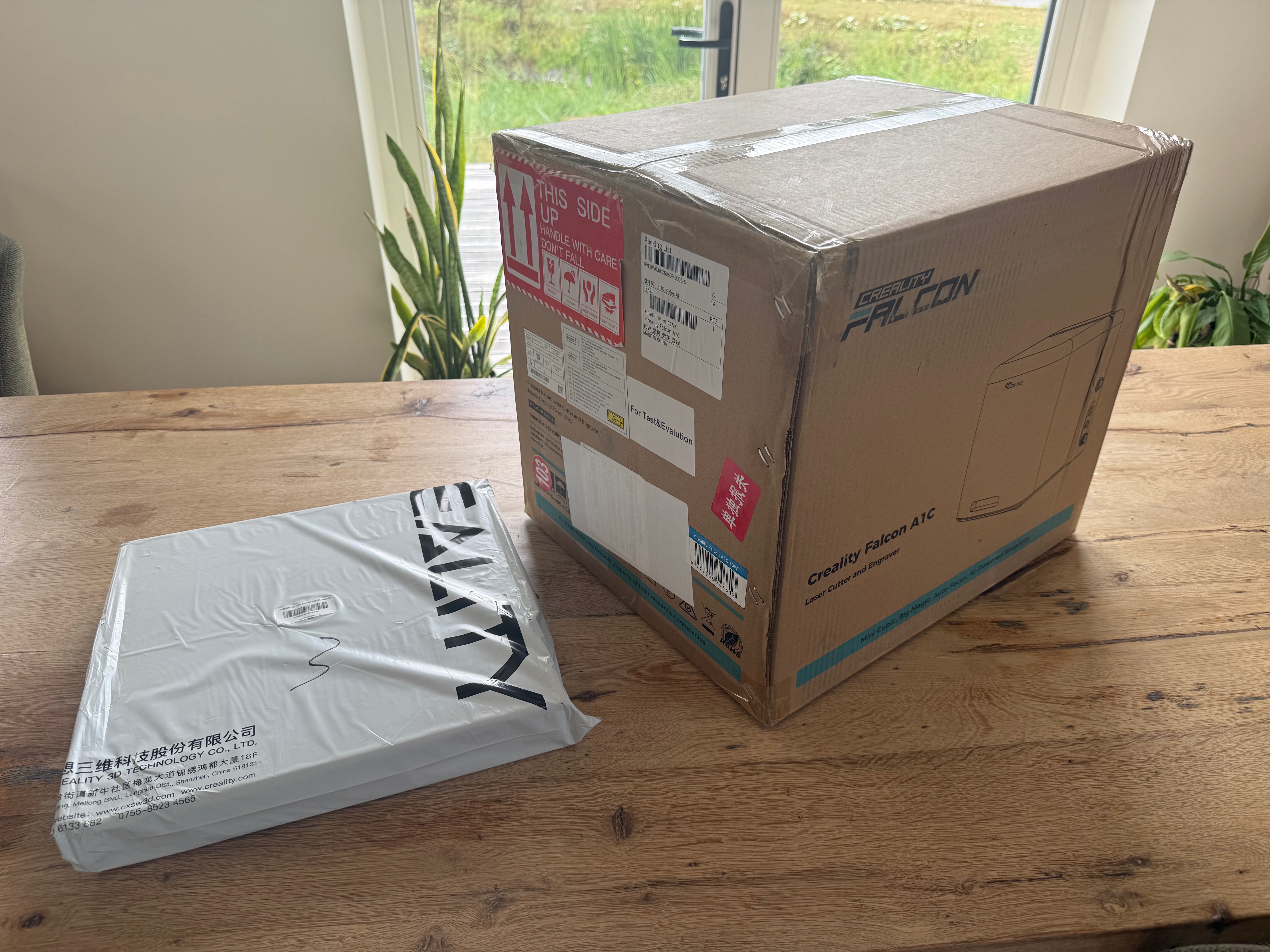 The sealed Creality Falcon A1C shipping box next to a separate Creality pack of plywood sheets