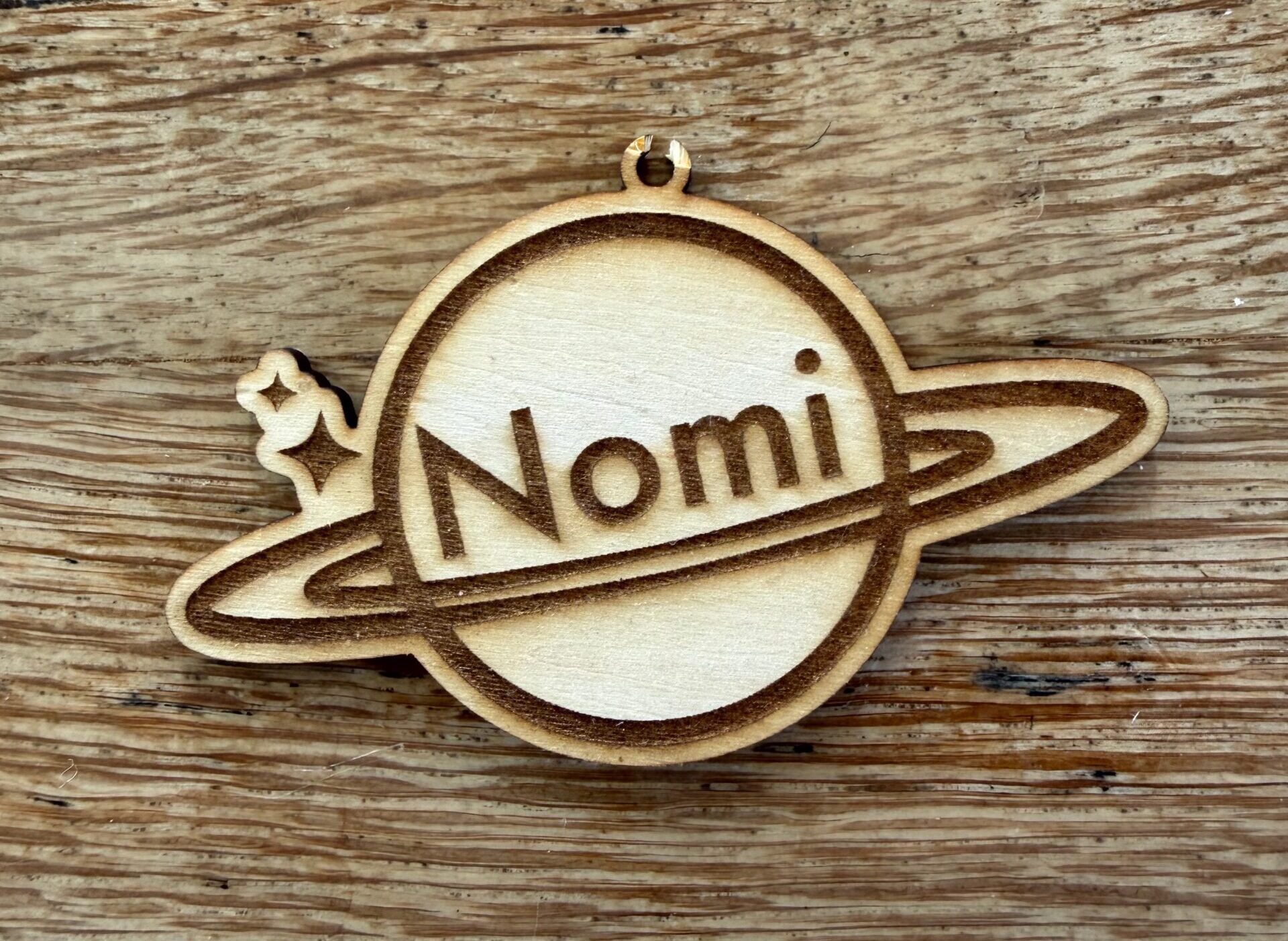 A small plywood keychain shaped like a ringed planet with a child's name engraved on it