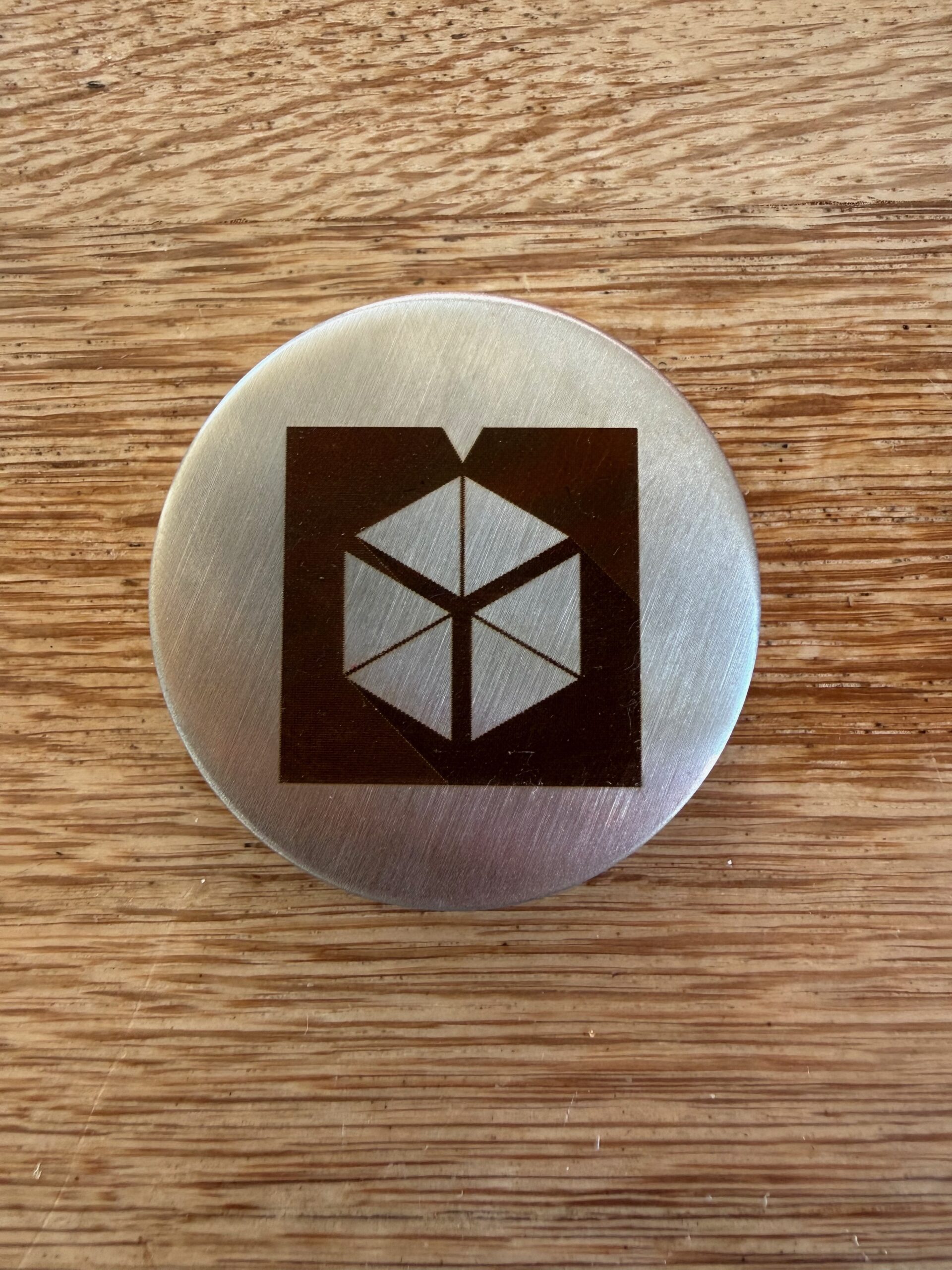 A round brushed stainless steel cover with a dark logo marked on it by the infrared laser module