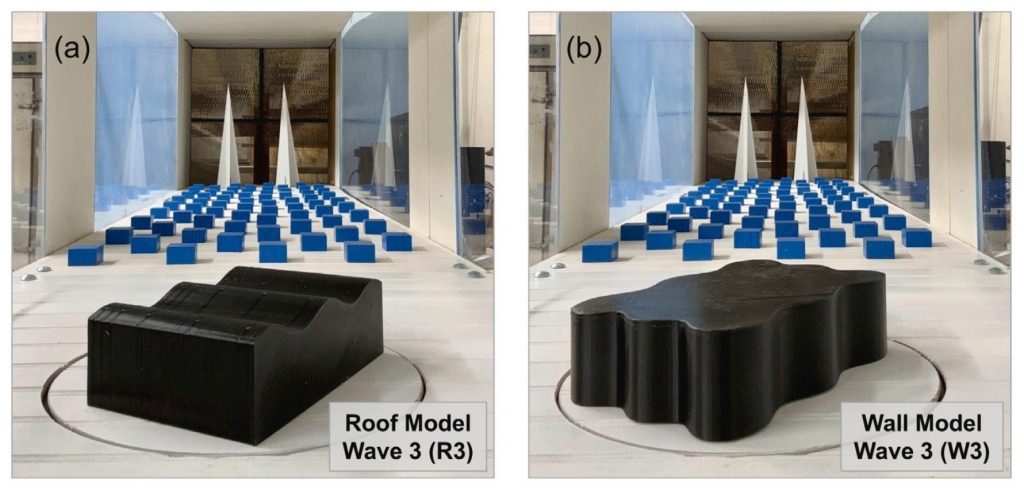 Two black 3D-printed building models in a wind tunnel, one with a stepped roof and one with wavy walls