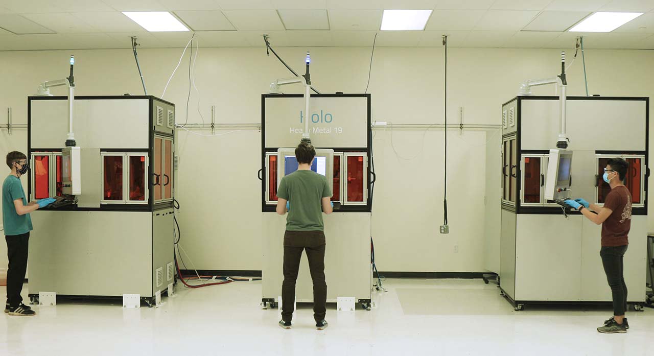 An operator working on one of the metal 3D printers in Holo's production fleet, with two more printers in frame.