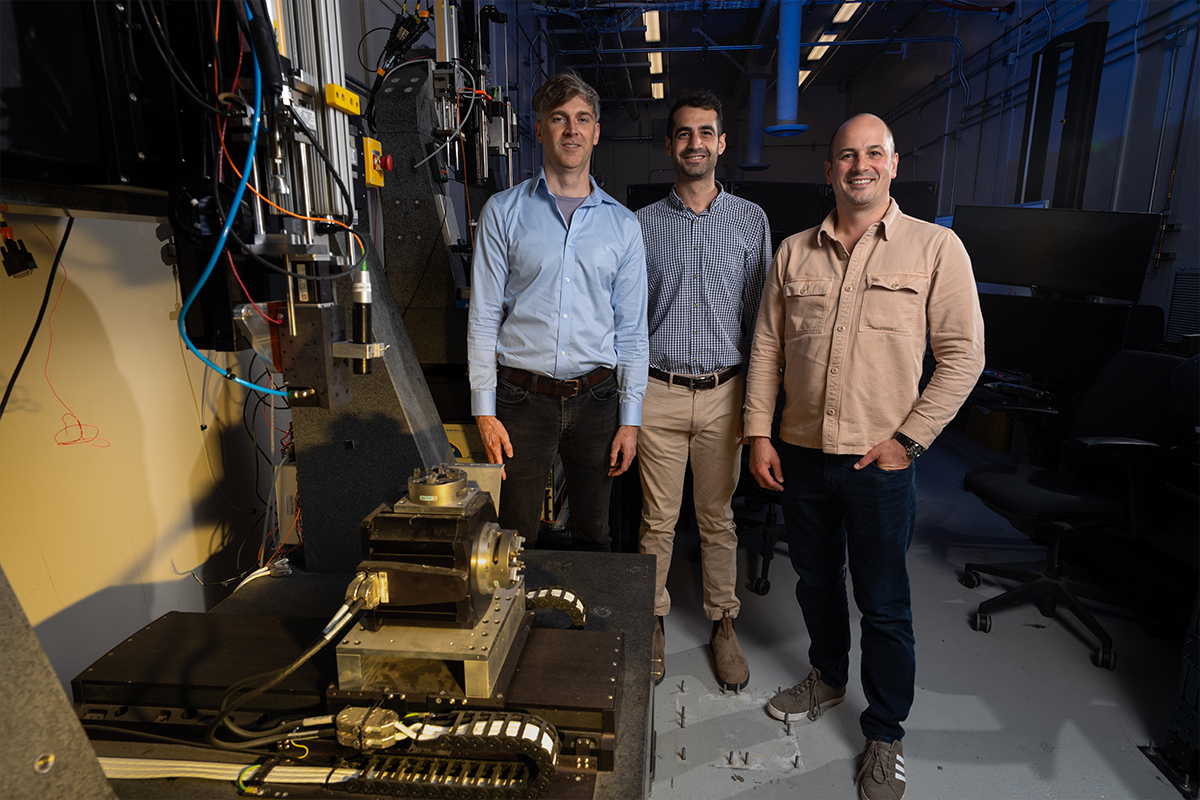 Three LLNL researchers standing beside a direct-ink writing 3D printer