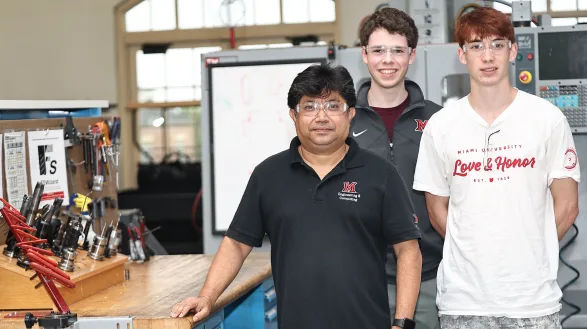 Three people stand in a lab with machine tools and CNC equipment behind them