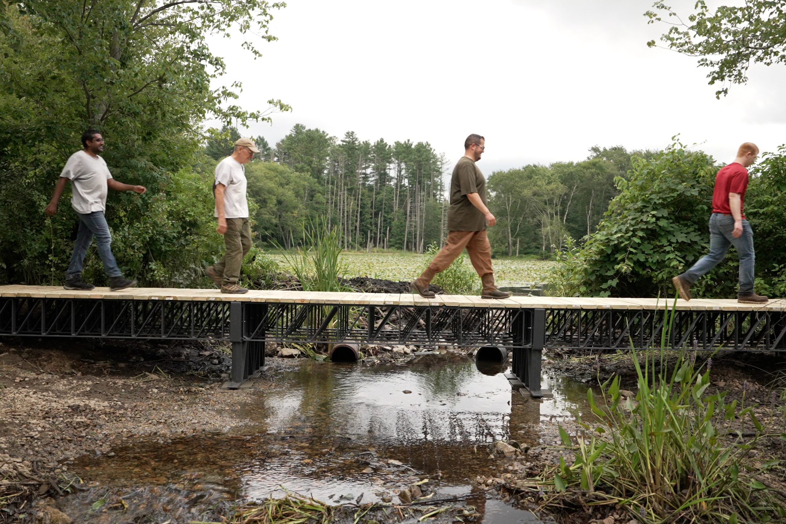 Four people walking across a 3D-printed recycled-composite wetland bridge
