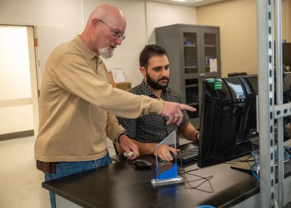 Samuel Larter points at a computer screen as Darren Mansour works at the keyboard, with an award on the desk in front of them