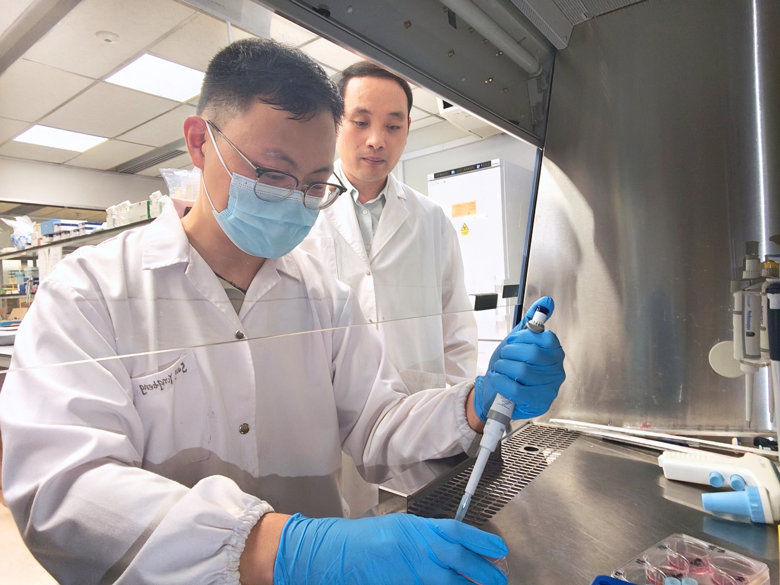 Yongteng Song pipetting in a lab while Associate Professor Changjin Huang watches