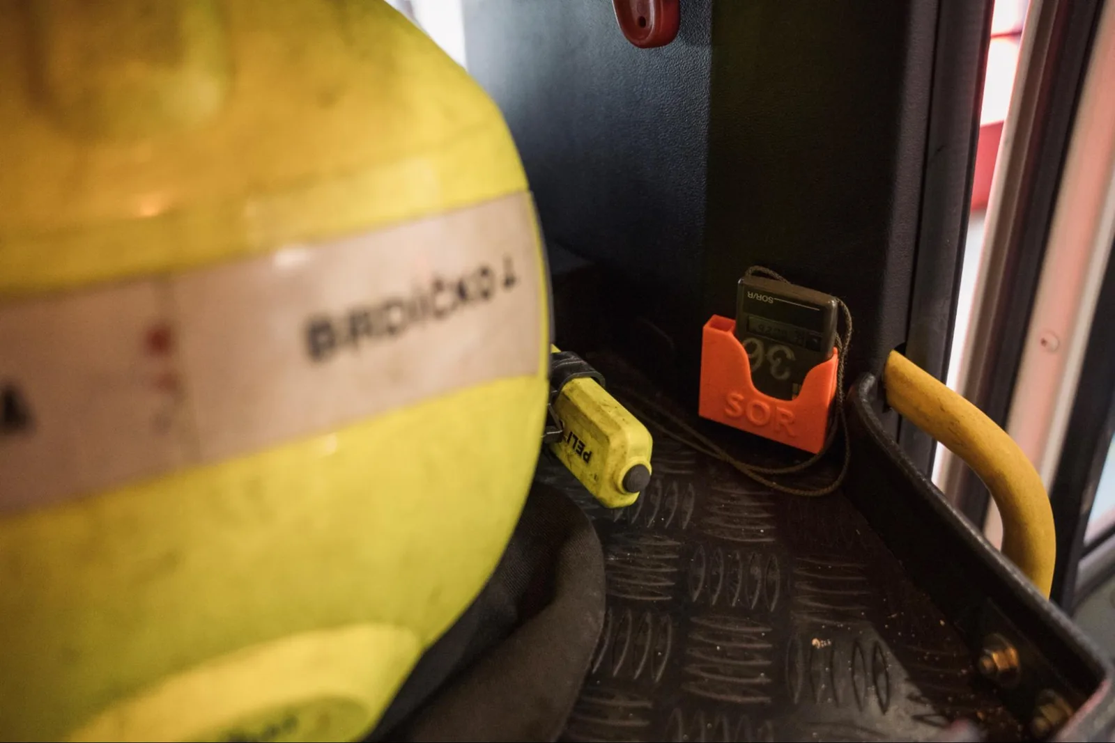 Orange 3D printed holder securing a handheld device inside a fire engine next to a firefighter helmet