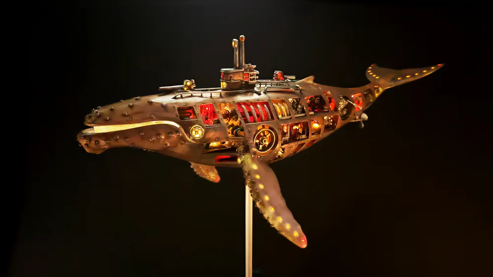 The finished whale sculpture on a stand against a black background, lit from inside with red and amber windows and small lights along its fins and tail