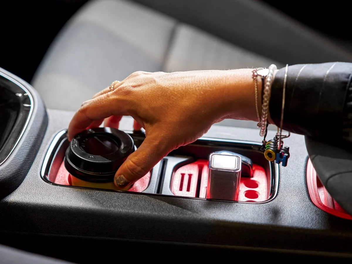 A hand placing a coffee cup into a printed cupholder insert in a Škoda Epiq