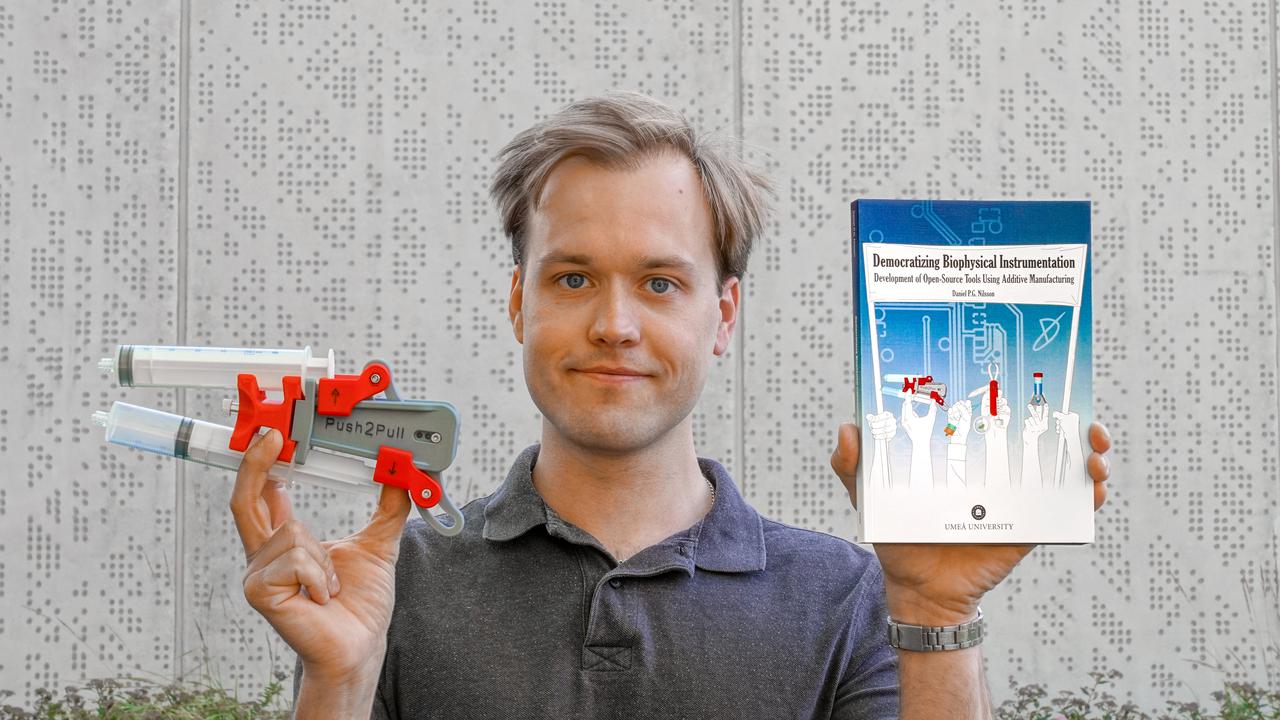 Daniel Nilsson holding a 3D-printed instrument fitted with two syringes and his doctoral thesis